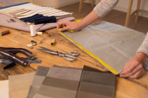 Close up hands of a fashion designer at work with cloth fabric. Professional tailor measuring textile material. Female hands at work with measuring tape for new cloth.